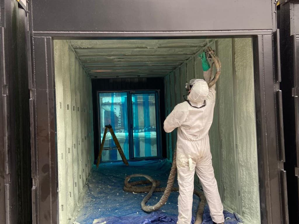 Technician applying spray foam insulation inside a shipping container