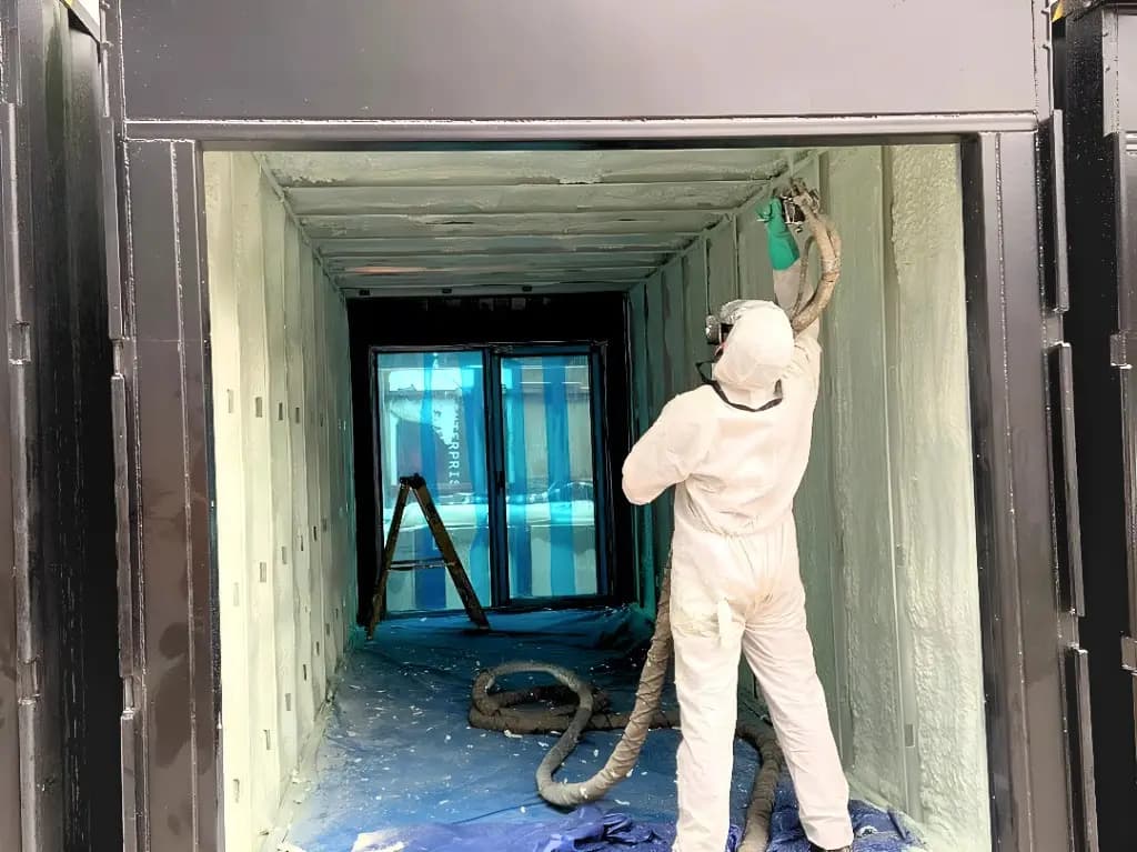Installer in protective suit spraying foam insulation inside a container